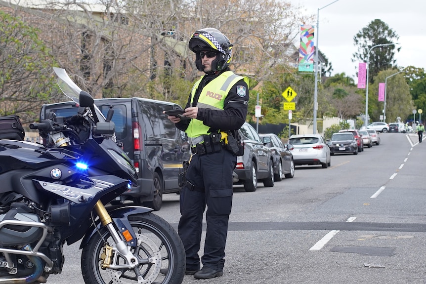 Queensland Police Service officer stands beside bike, closing River Terrace at scene of shooting in Kangaroo Point