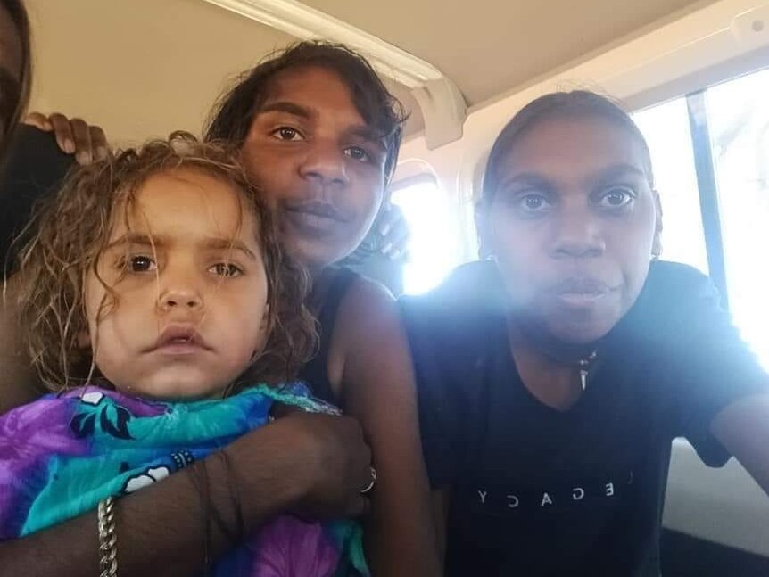 Une fillette de quatre ans qui a passé plus de 24 heures à disparaître dans le désert regarde la caméra d'un air vide avec deux jeunes filles souriantes