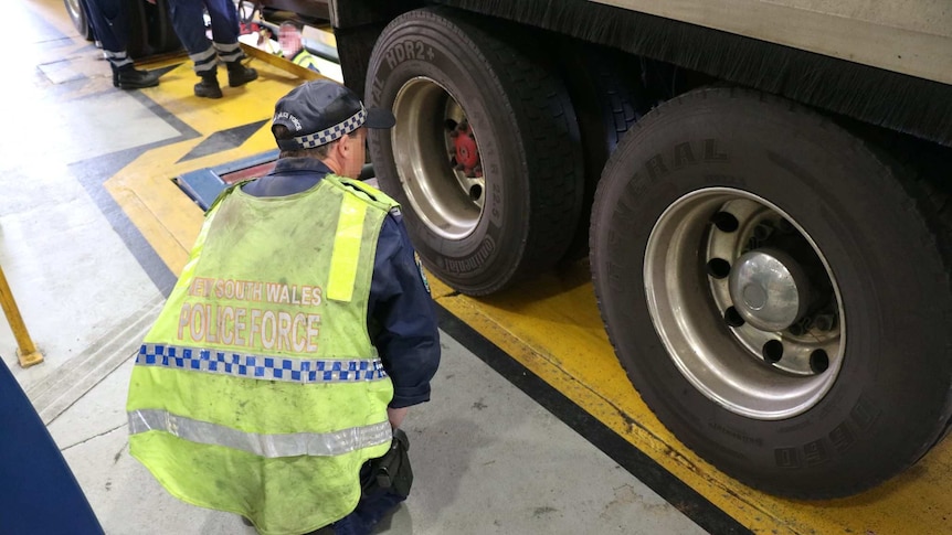 A police officer inspects the wheels of a truck.
