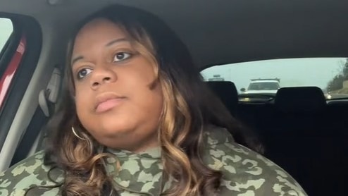 A black woman sits in a car, she's looking away from the camera, she looks frustrated.