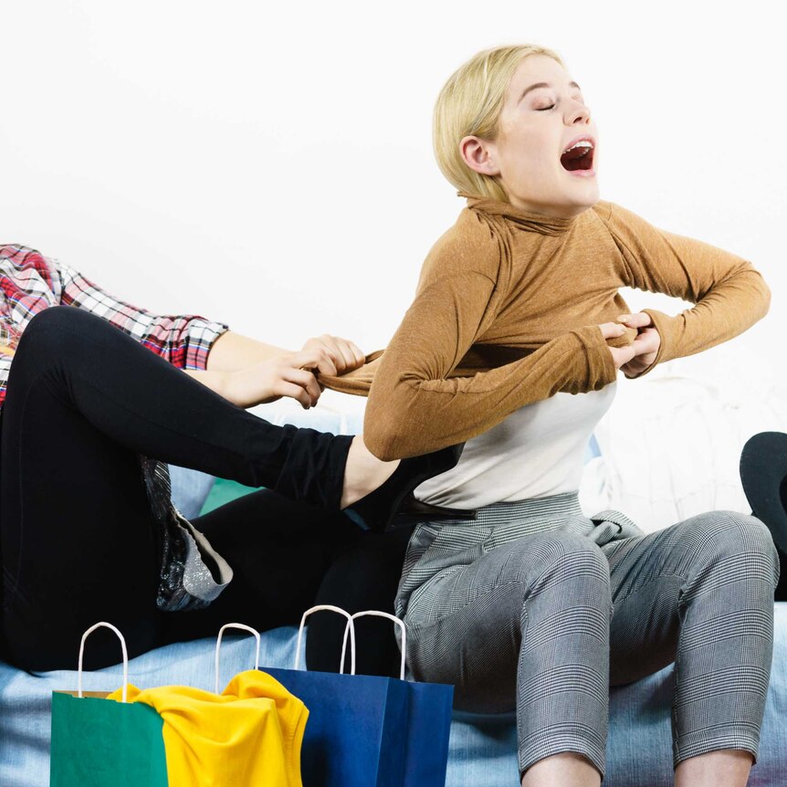 One woman dragging at the jumper of another woman surrounded by shopping bags