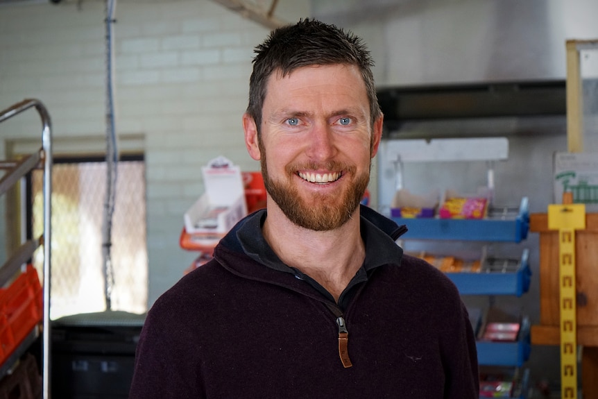 A tall man in a purple jumper smiles at the camera