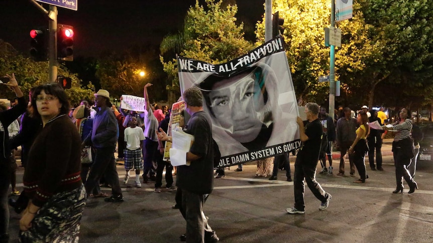 Protesters hold up a banner reading "We are all Trayvon. The whole damn system is guilty."