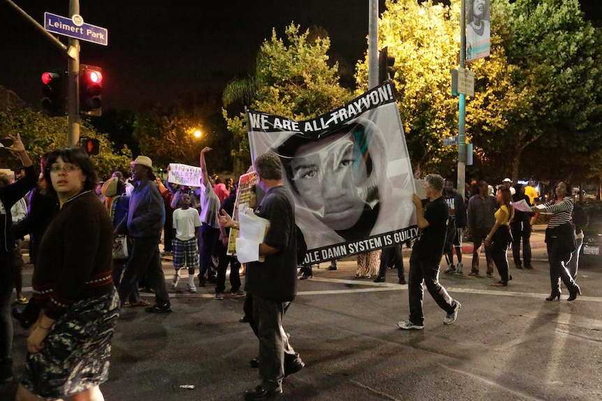 Protesters hold up a banner reading "We are all Trayvon. The whole damn system is guilty."