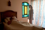 A man lying in bed and a ghost woman watching him