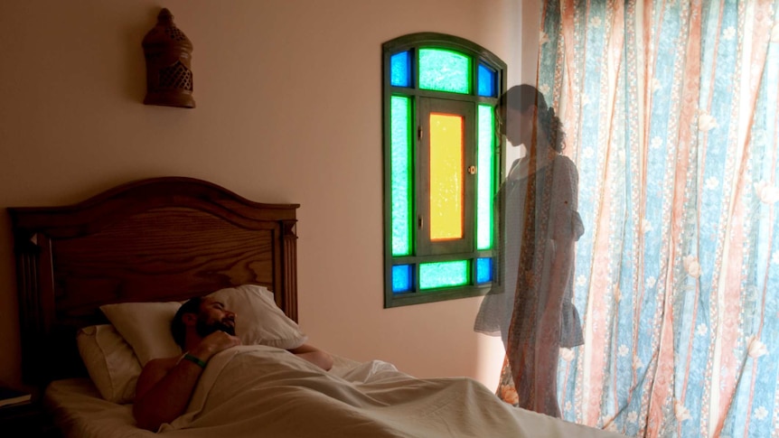 A man lying in bed and a ghost woman watching him