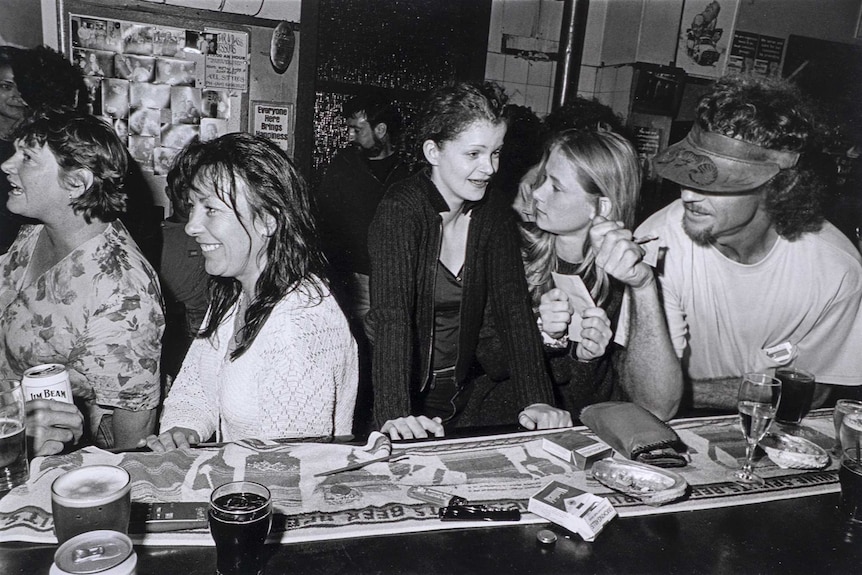 Black and white photo shows revellers in a packed bar.