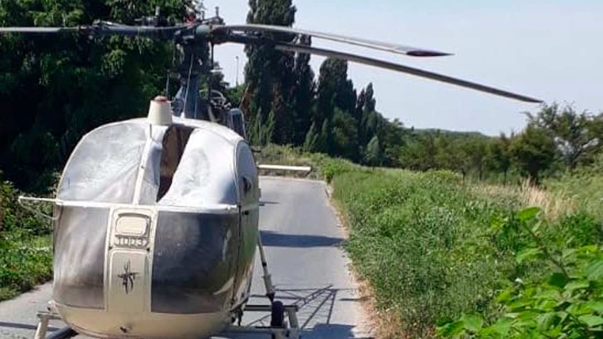 Burnt out helicopter sits on small road between fields