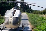 Burnt out helicopter sits on small road between fields