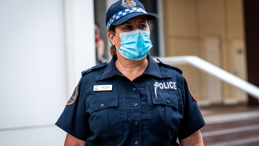 A woman in a navy police officer's uniform wearing a surgical mask standing outside a beige building