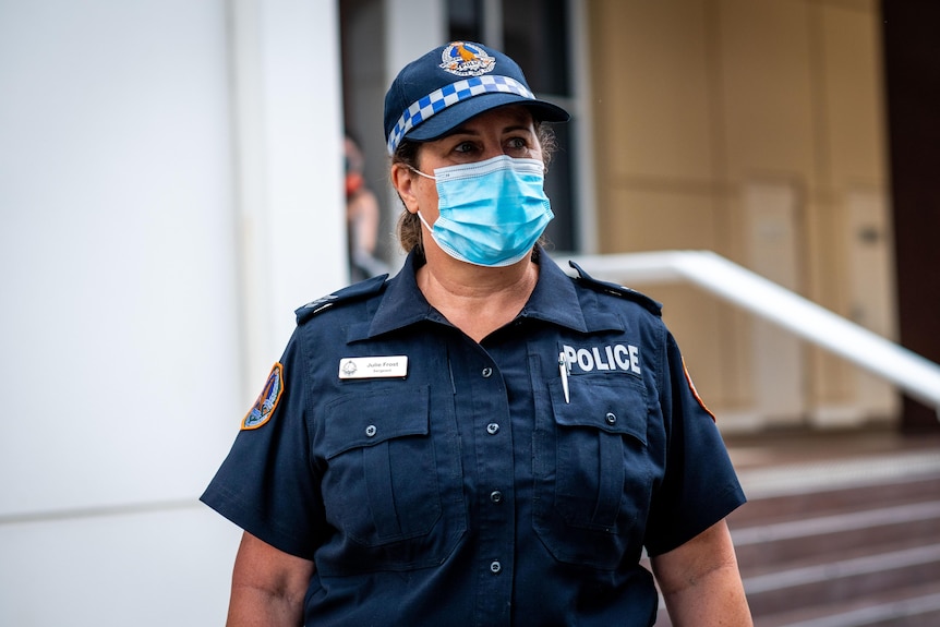 A woman in a navy police officer's uniform wearing a surgical mask standing outside a beige building