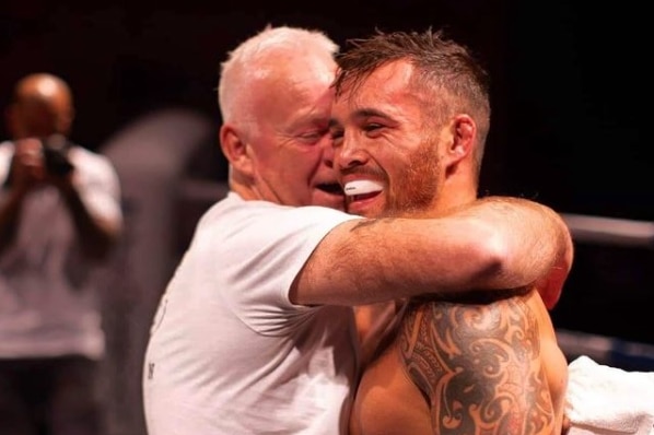 Bowyn Morgan is hugged by a man in a white t-shirt, both are smiling, in a boxing ring