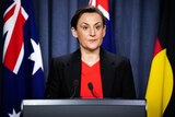 Woman with short brown hair speaking at a lectern in front of the Australian, Western Australian, and Aborignial flags.