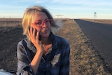 Shanna Whan, creator of Sober in the Country, standing on the side of the highway with a phone to her ear.