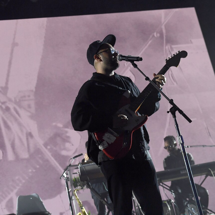 Ruban from Unknown Mortal Orchestra standing at a microphone playing a guitar