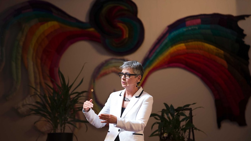 A woman wearing a white jacket gestures as she speaks to a congregation.