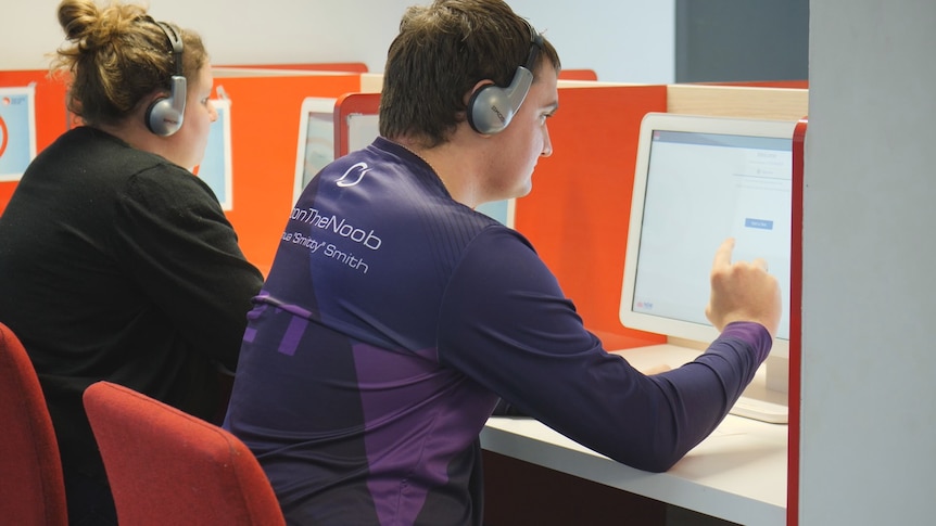 A young man takes a test using a computer. There is a woman sitting to his left