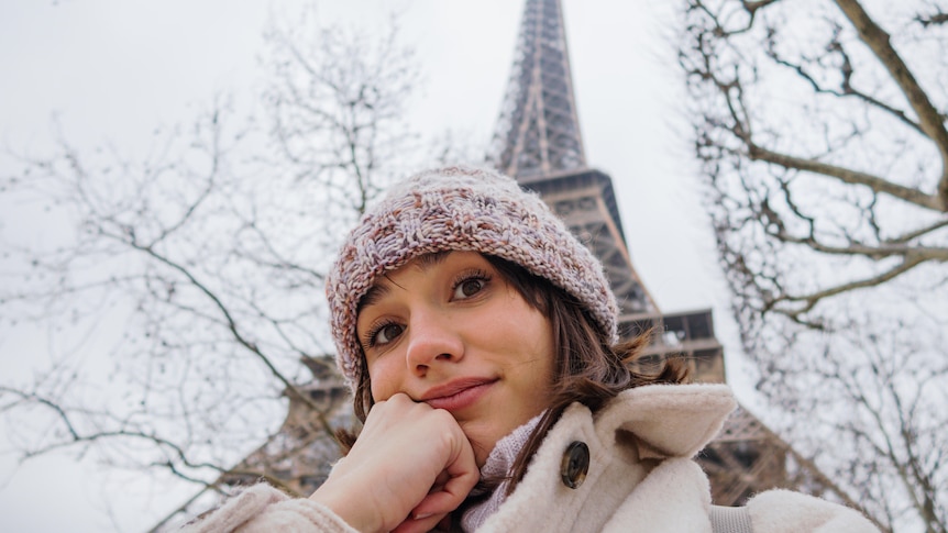 A selfie of a woman with a bemused expression under the Eiffel Tower