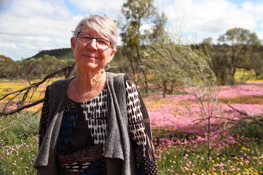 Wildflower enthusiast Glenda Blythe standing in front of yellow and pink wildflowers at Coalseam Conservation Park