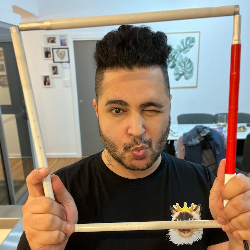 A man poses with a wink as he hold his deconstucted cane around his face like a frame.