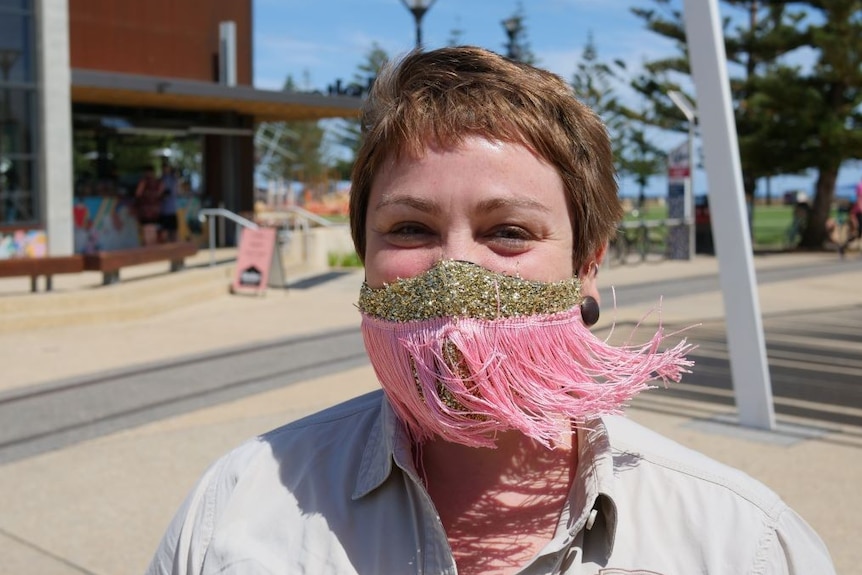 A woman wears a pink mask with tassels on a waterfront