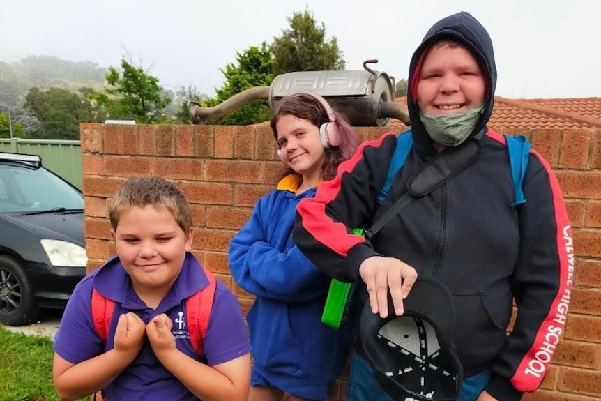 Three kids smile with their backpacks on. 