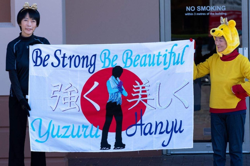 Two women, one dressed as Winnie the Pooh, hold a banner supporting figure skating star Hanyu Yuzuru.