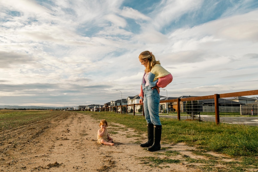 A mother watching her toddler play in a vacant lot