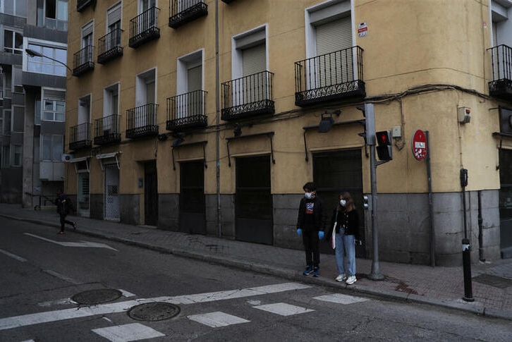 A young man and woman wait to cross an empty street in Madrid Spain.