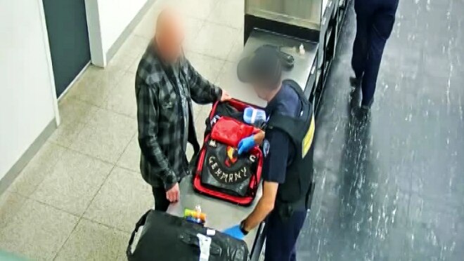 A shot from a CCTV camera on a ceiling showing a bikie gang member at a customs desk at Perth Airport with a border official.