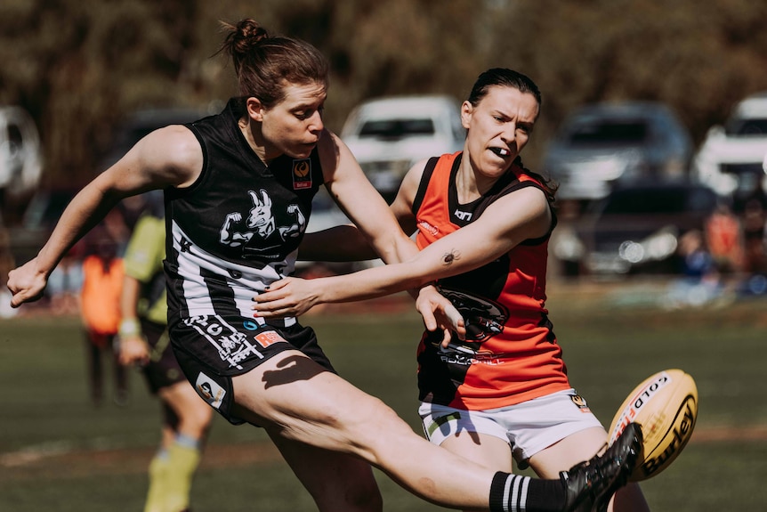 Two female football players in action as one kicks the ball and the other tackles