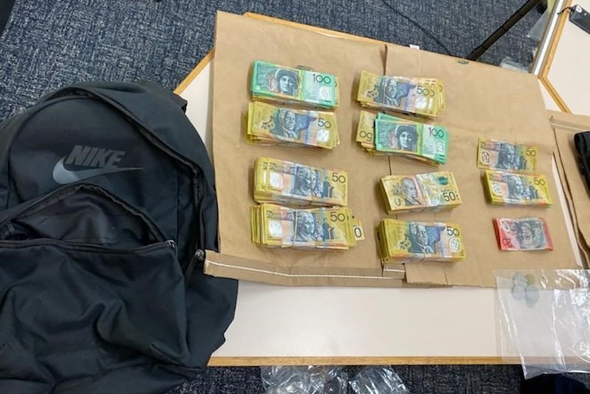 Queensland police display bundles of cash on a table and a backpack seized in a criminal operation.