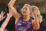 A netballer jumps up and extends her arm as she prepares to pass over the defence.