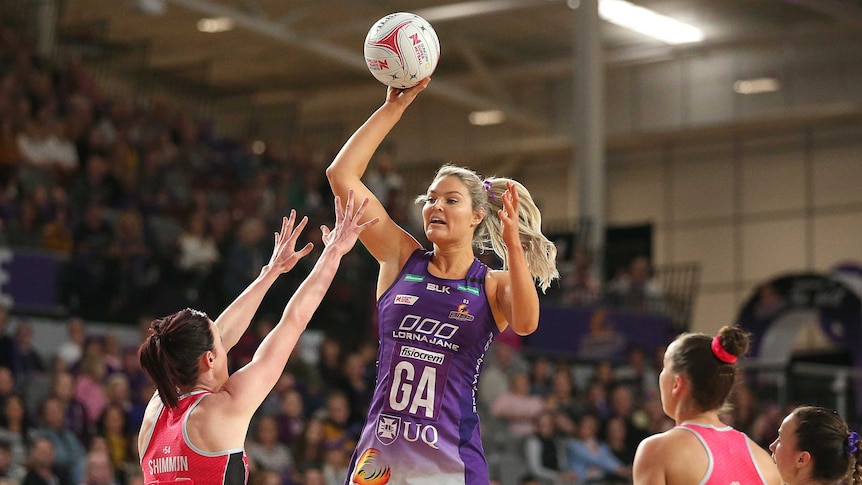 A netballer jumps up and extends her arm as she prepares to pass over the defence.