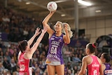 A netballer jumps up and extends her arm as she prepares to pass over the defence.