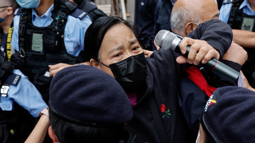 a woman holding a microphone is held back by police outside West Kowloon Magistrates' Court