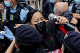 a woman holding a microphone is held back by police outside West Kowloon Magistrates' Court