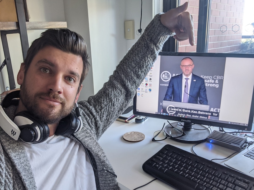 A man with a white headset around his neck points to his computer with the mistake on it