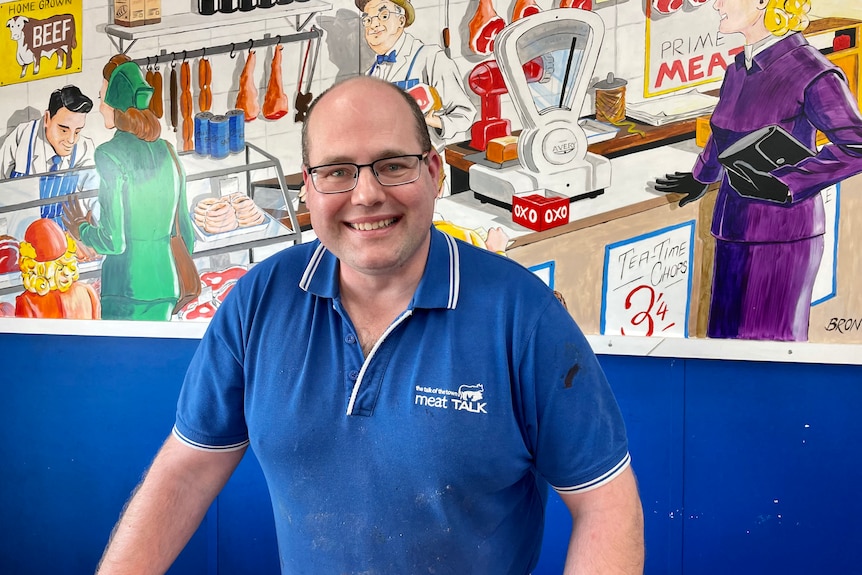 A man in blue shirt stands infront of a mural 