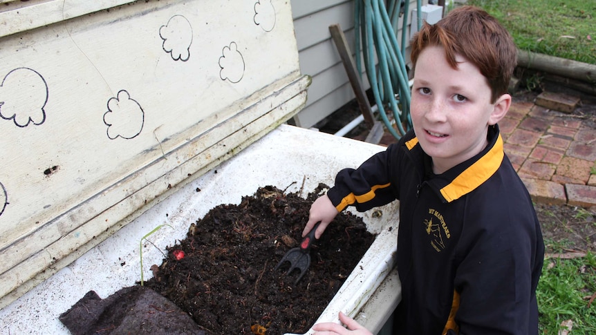 A young boy kneeling next to a bathtub full of dirt and worms