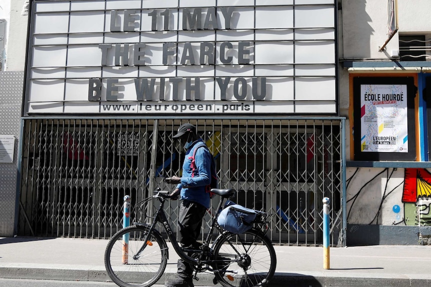 A cyclist passes by a sign for a closed theatre