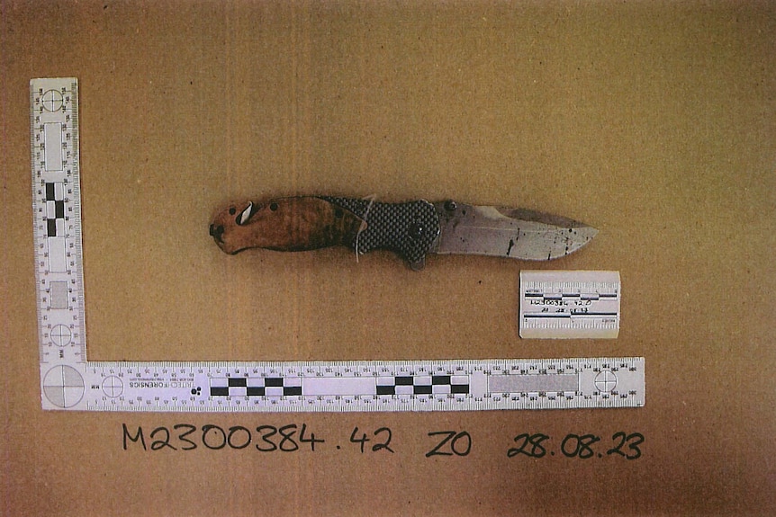 A picture of a small knife with a trace amount of blood by a measuring tape.