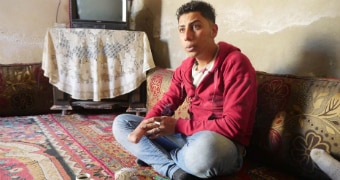 A man sits on a carpet, revealing the stump where his right hand was amputated.