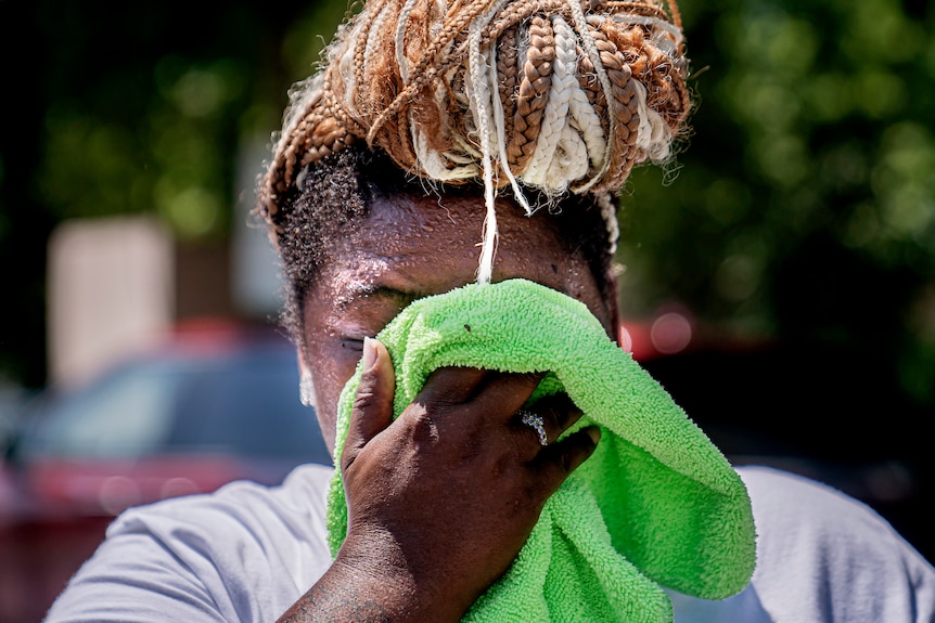 A woman with braids in a bun on her head wipes sweat from her face with a hand towel.