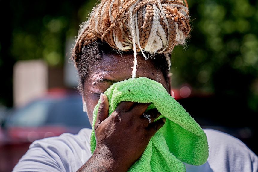 Una mujer con trenzas en la cabeza se limpia el sudor de la cara con una toalla de mano.