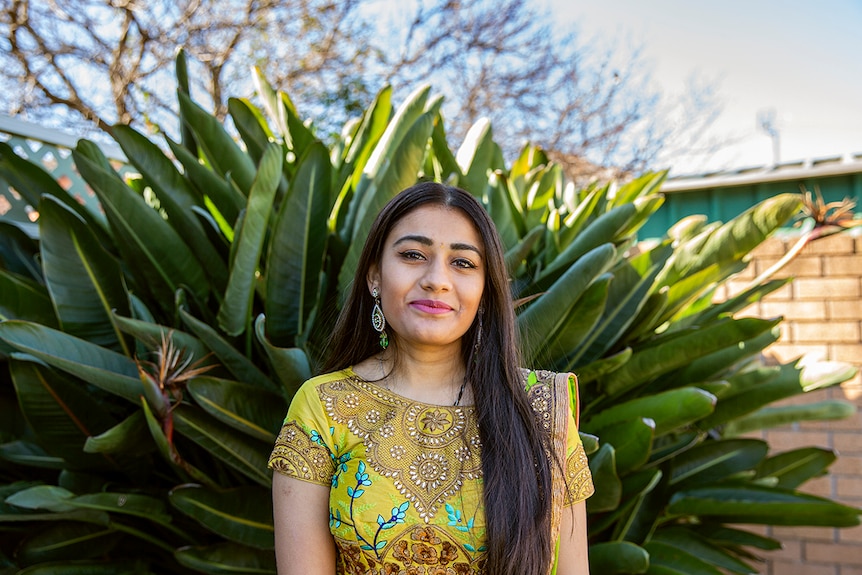 Meera Patel standing in yard in front of birds of paradise, wearing traditional Indian clothing and jewellery.