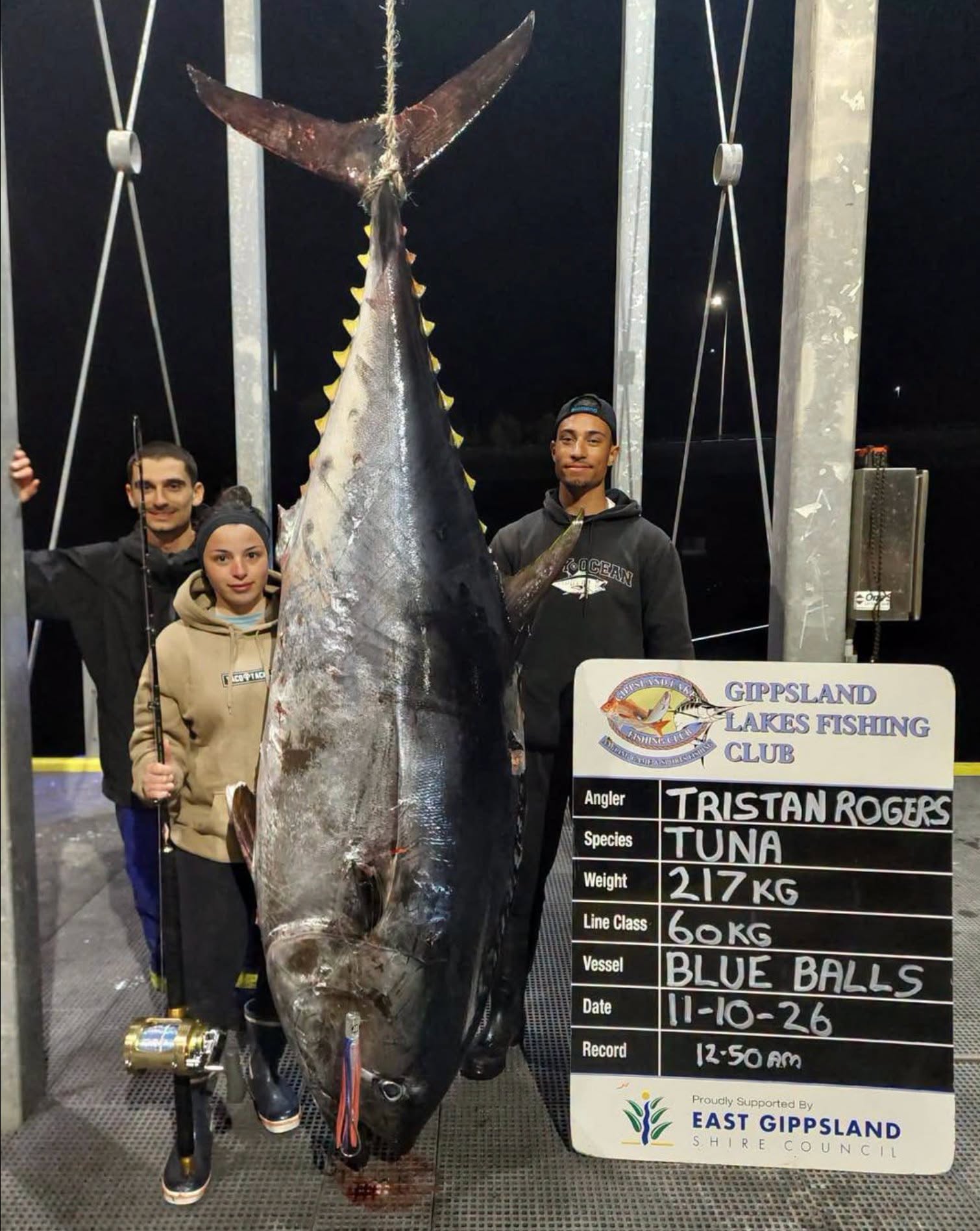 A group of three people, standing on a jetty at night, with a giant tuna fish next to them