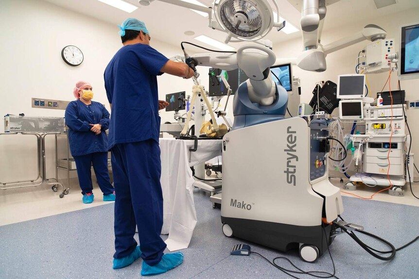 A hospital room with a doctor and nurse in scrubs and facemasks operate with a robot machine