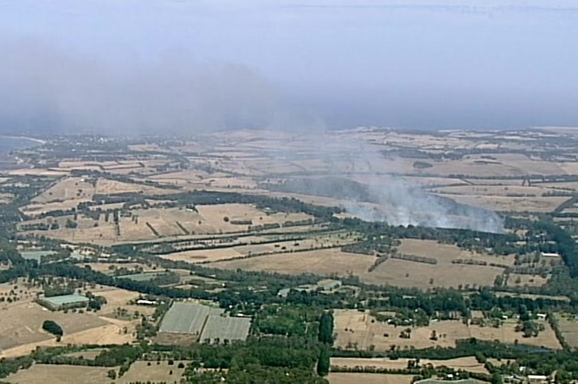 An aerial shot of smoke coming from trees surrounded by paddocks.