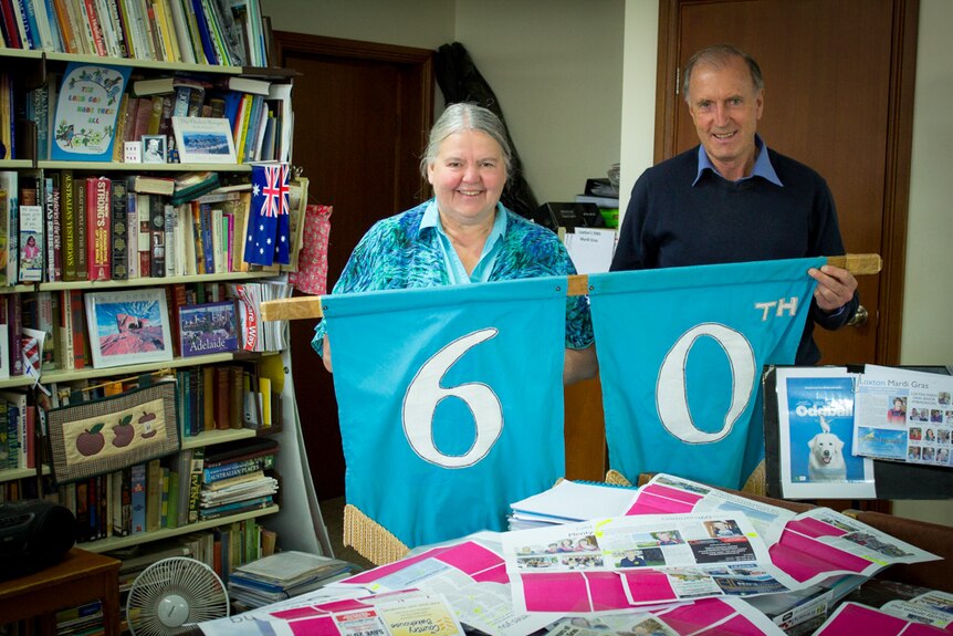 Carla and Peter Magarey in their home holding up a banner saying 60th.